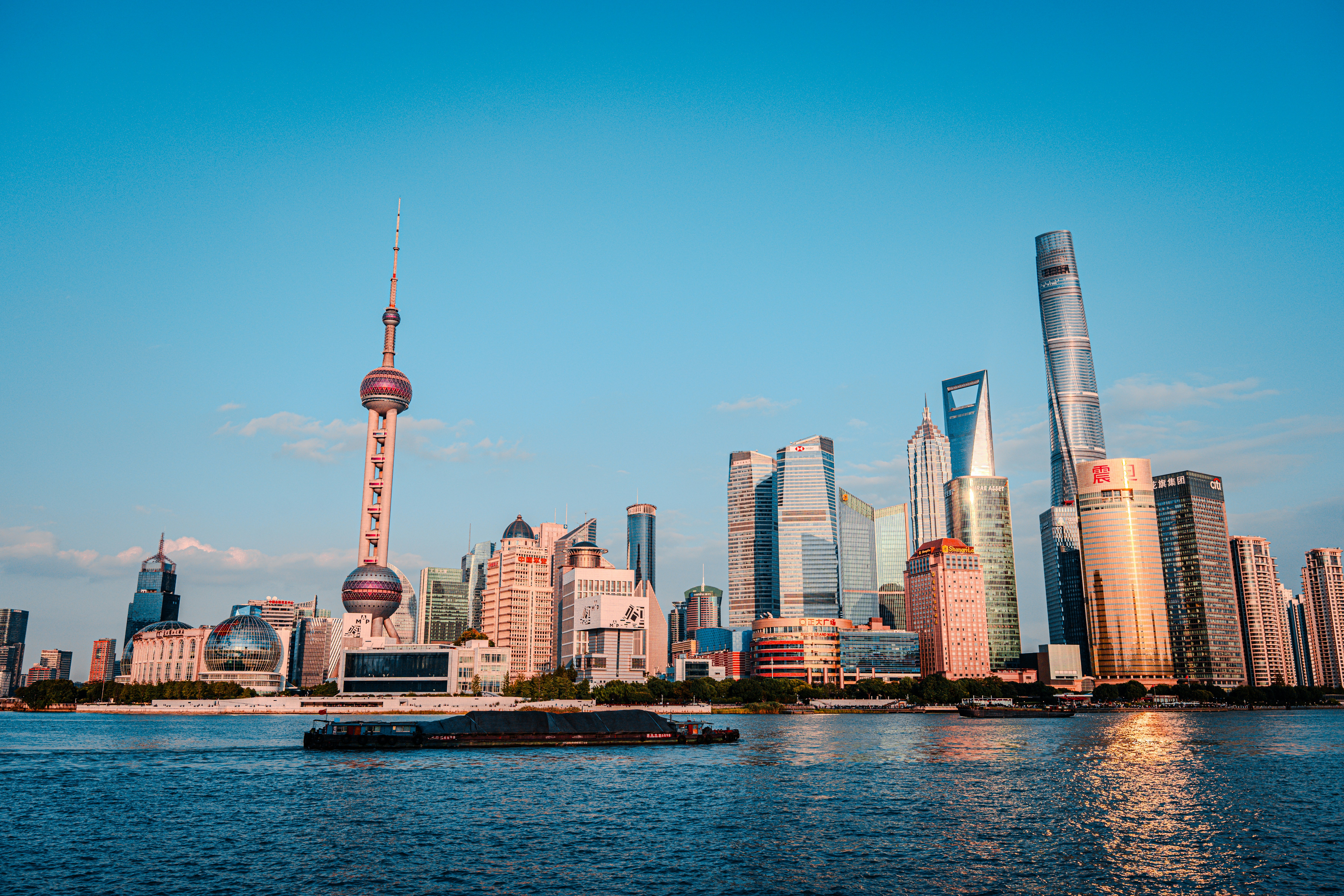 Daytime view of Lujiazui skyline from the Bund — Oriental Pearl Tower on the left, three super-tall towers on the right, with a barge on the Huangpu River