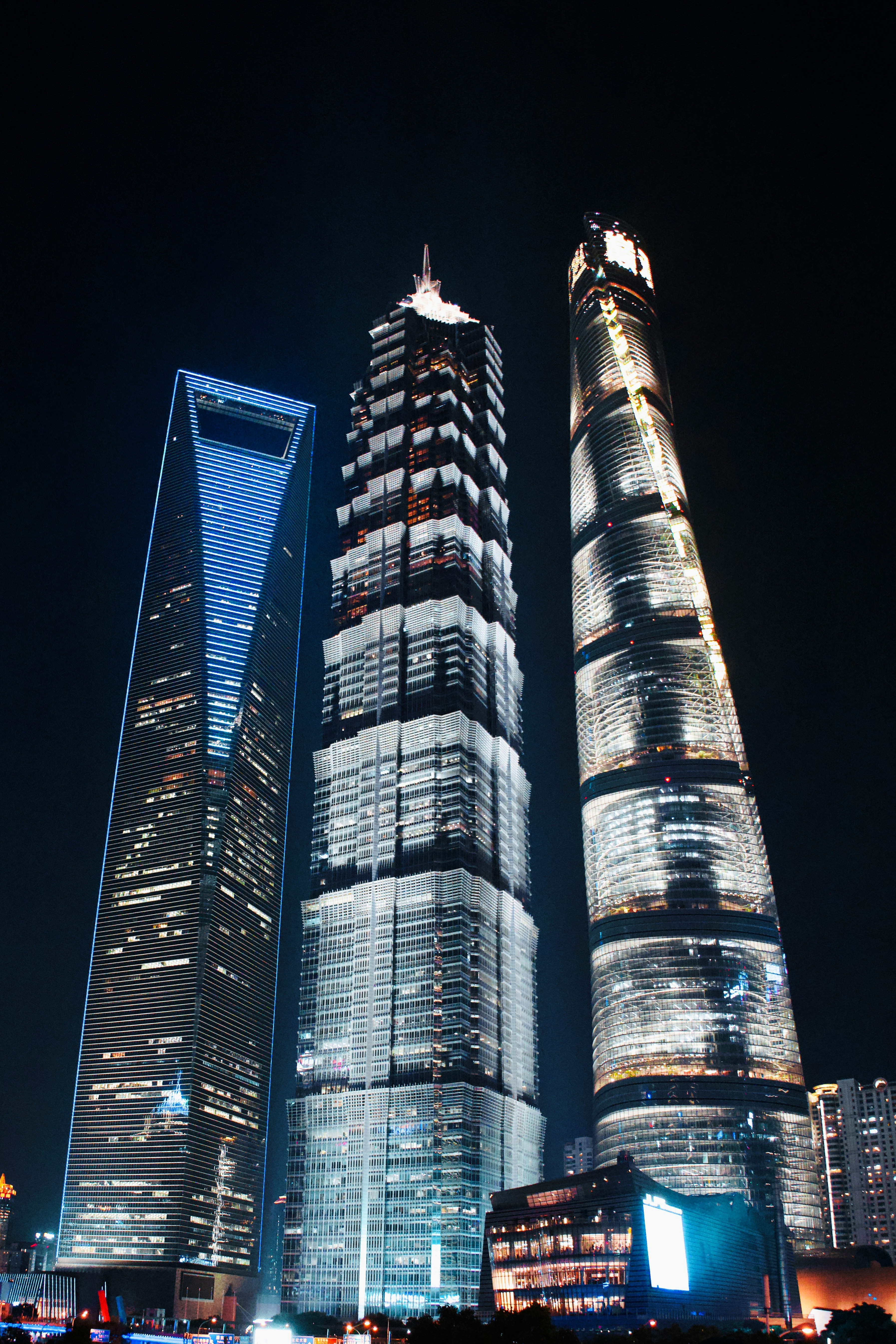 Three Lujiazui towers at night seen from below — SWFC, Jin Mao, and Shanghai Tower stacked next to each other