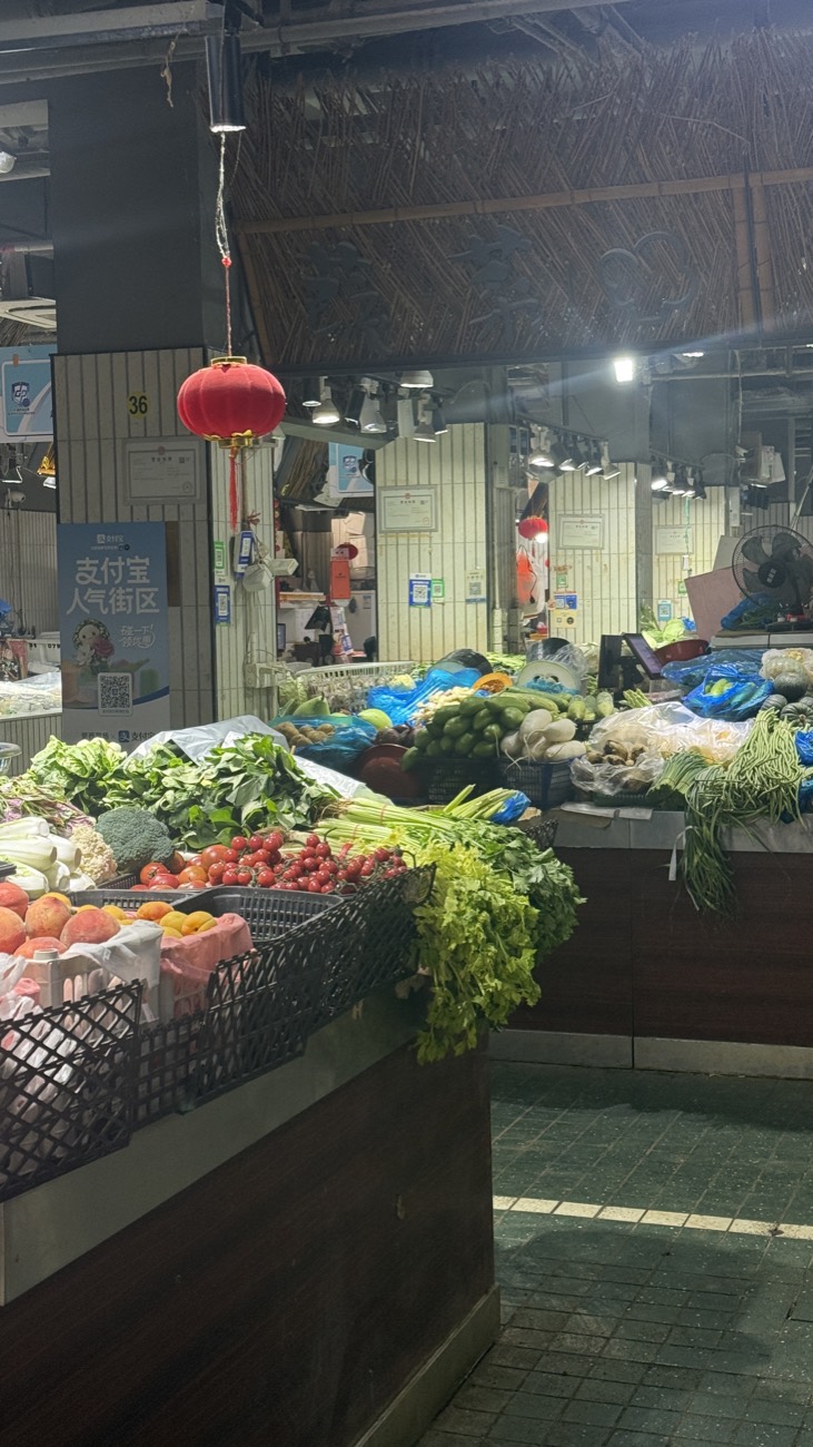 Inside Mengxi Market — produce stalls under warm light with a red lantern hanging from the bamboo-lined ceiling