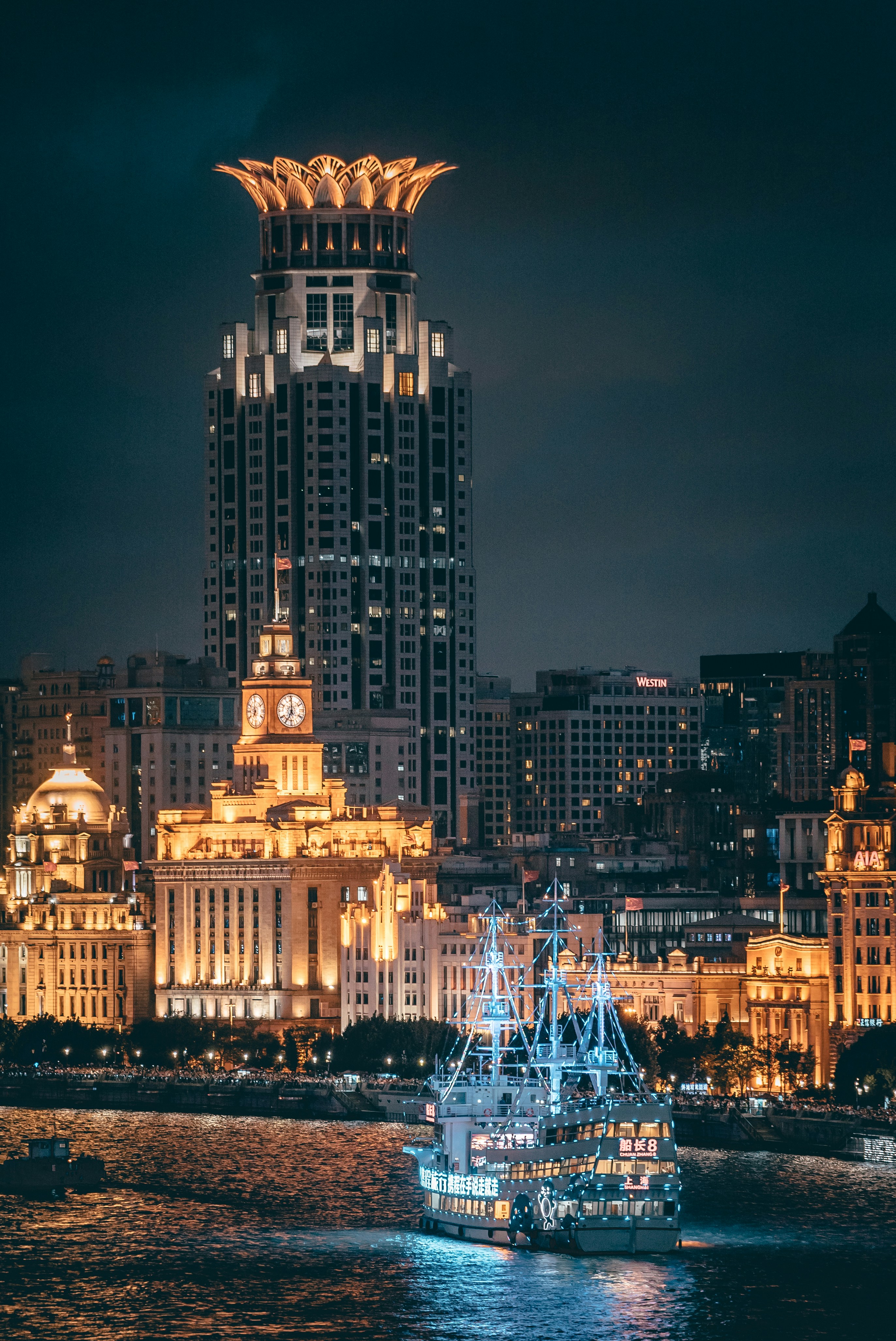 The Bund at night — Art Deco crown lit gold, with a tourist boat on the Huangpu