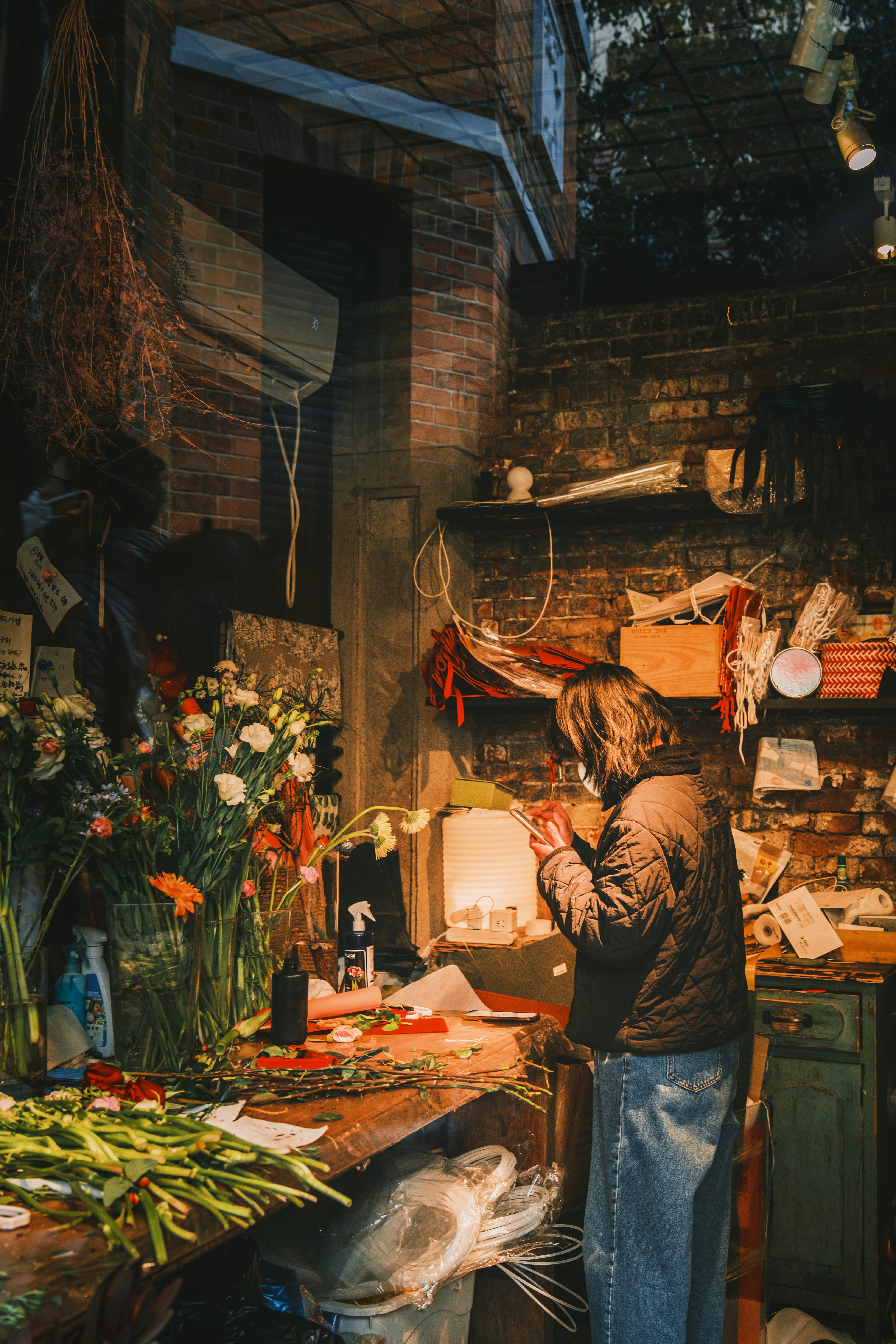 Florist working in a brick-walled indie shop near Anfu Road — flowers, warm tungsten light, the contemporary half