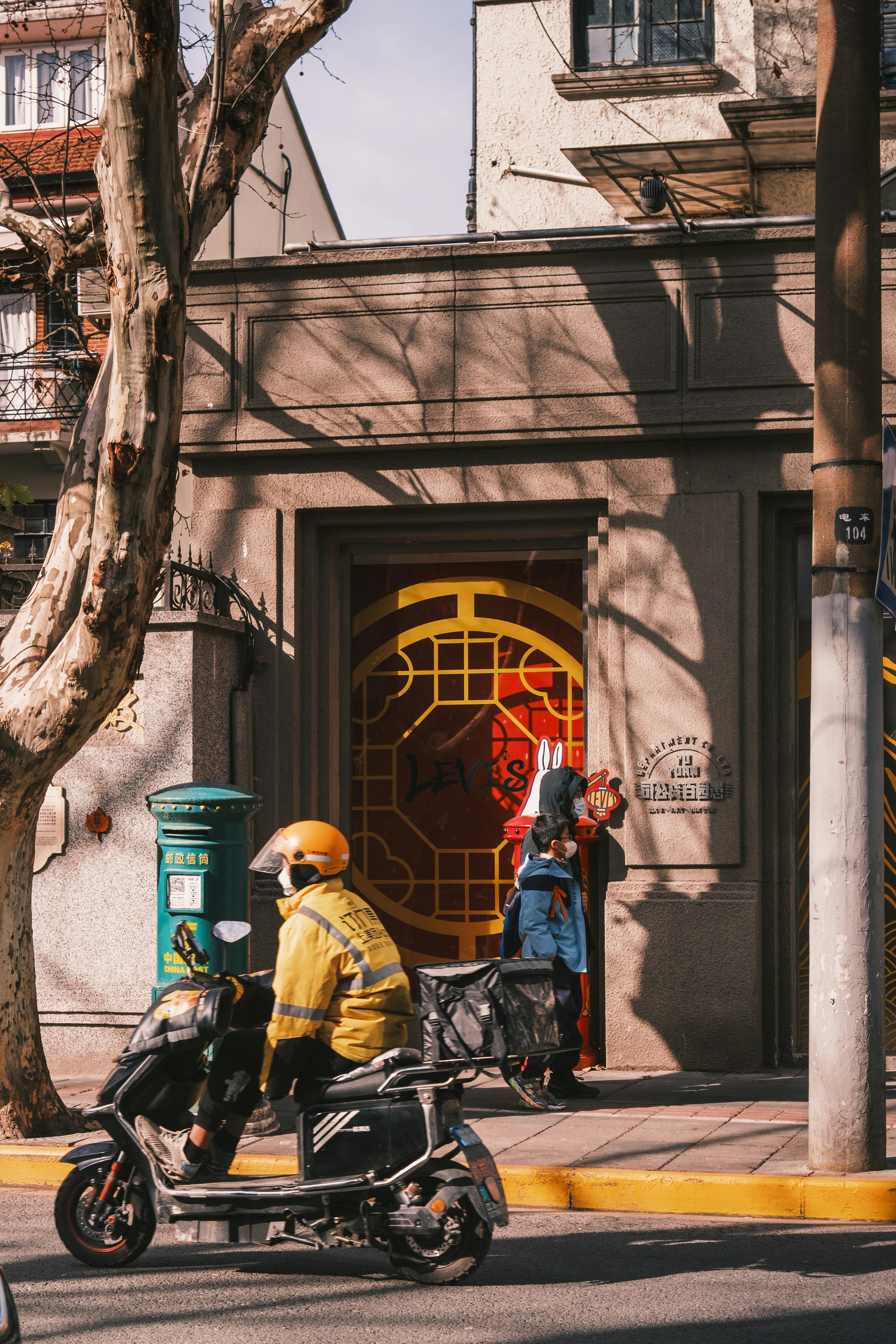 A French Concession Art Deco doorway on Wukang Road, golden hour, delivery rider passing — heritage half of the walk